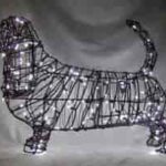 Wire frame topiary of a Basset Hound wrapped in glowing mini lights, low-angle view.