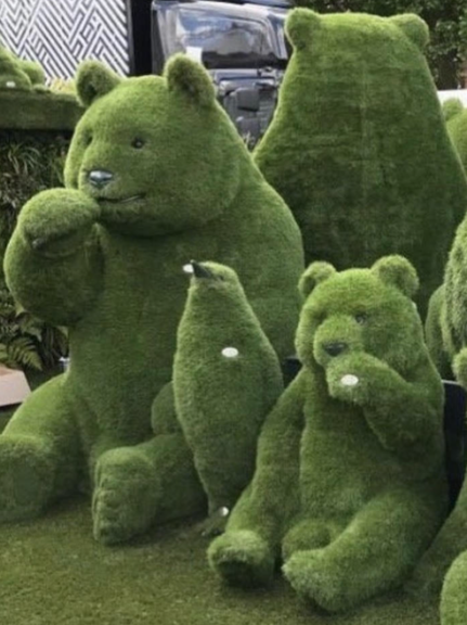 A group of green bear-shaped topiaries of different sizes with a bird-shaped topiary, staged outdoors