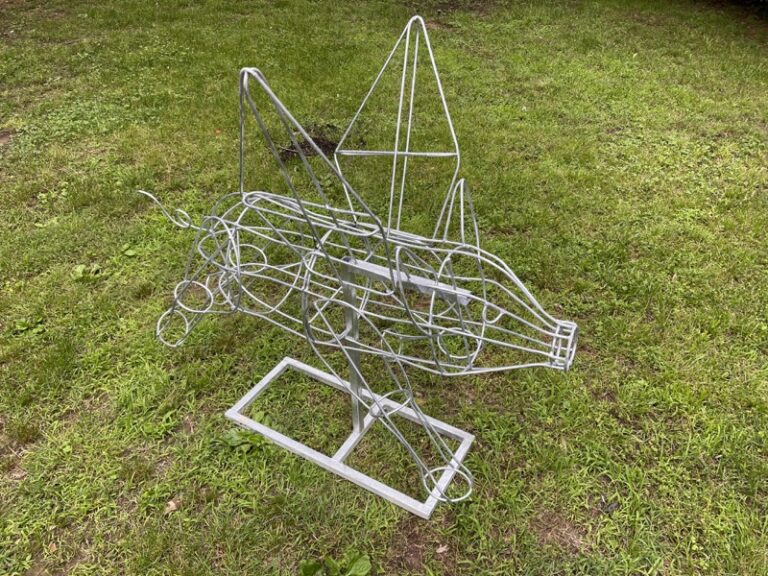 Bare wire flying-pig topiary frame on a metal stand, leaping pose, before moss fill