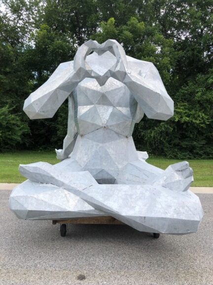 Bare galvanized steel figure sculpture making a heart shape with its hands, outdoors