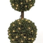 Three-ball pine topiary lit with warm white lights on a brown trunk, standing in a black plastic pot