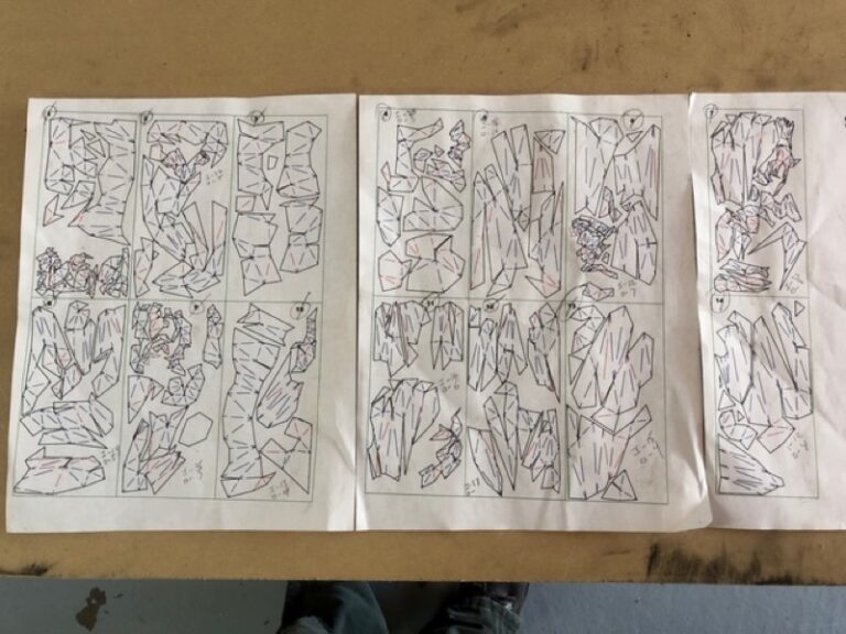 Hand-drawn paper panel templates for the steel frame, laid on a workbench