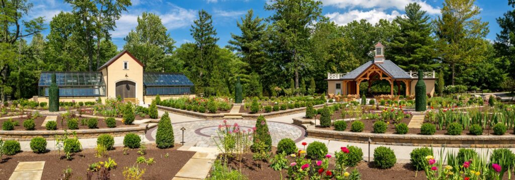 Wide view of a landscaped garden estate with a tall bottle-shaped topiary near a pavilion