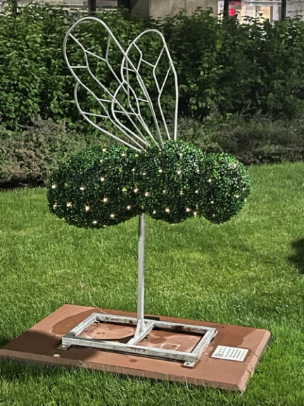 Bumble bee topiary with clipped green foliage body, wire wings and small lights, on a paver base