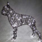 Wire frame topiary of a Boston Terrier wrapped in glowing mini lights at night.