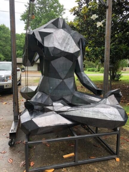 Galvanized steel figure sculpture suspended from a hoist, close view