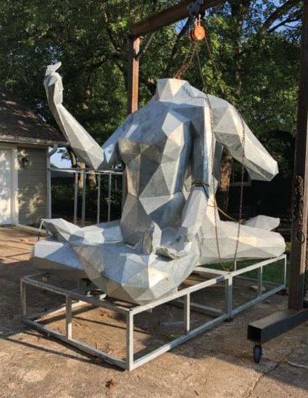 Galvanized steel figure sculpture suspended from a hoist, one arm raised