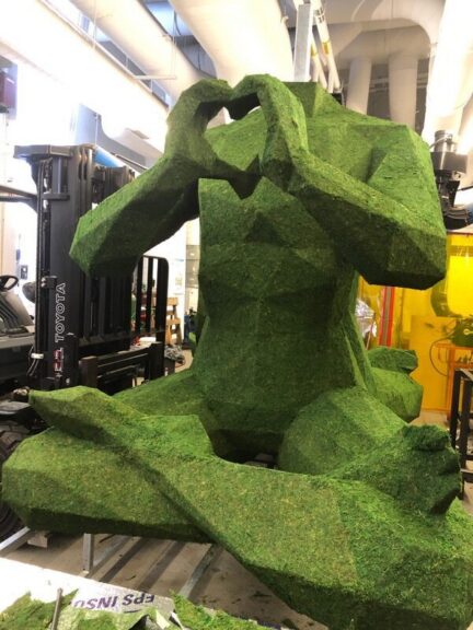 Moss-covered seated figure sculpture making a heart shape with its hands