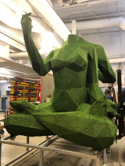 Moss-covered seated figure sculpture with one arm raised