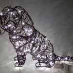 Wire-frame Cavalier Spaniel topiary sitting, wrapped in warm white miniature lights, long drooping ears visible