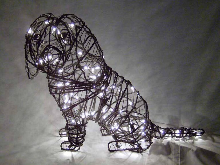 Wire-frame Cavalier Spaniel topiary sitting, wrapped in warm white miniature lights, long drooping ears visible