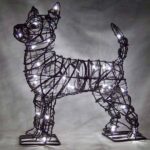 Wire chihuahua topiary frame lit with clear miniature bulbs, standing on flat metal base plates