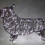 Corgi topiary frame in dark wire wrapped in lit white mini lights, glowing against a grey backdrop