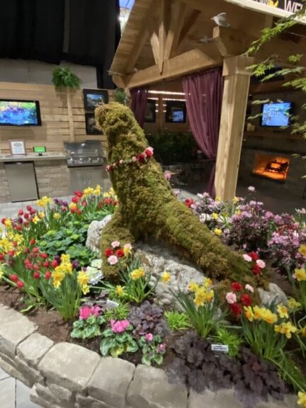 Moss-covered seal topiary on a stone base among tulips and daffodils at an indoor display