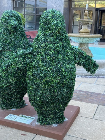 Close-up of two penguin-shaped topiaries covered in green foliage, with a small sign mounted at their base