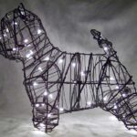 Wire-frame Westie topiary lit with warm white miniature lights, upright ear and short raised tail, dark background