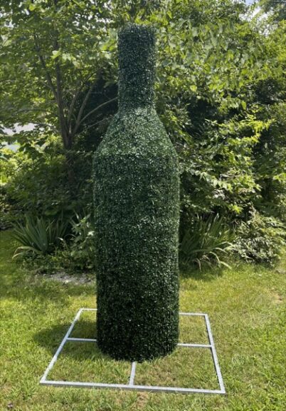 Tall bottle-shaped topiary covered in clipped green foliage in a garden bed