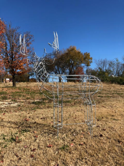 Bare welded steel deer frame with antlers, standing in a field with autumn trees behind