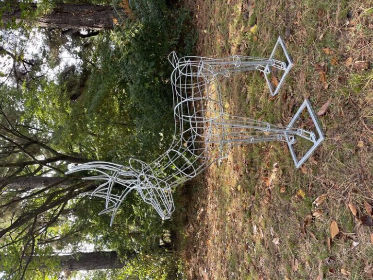 Welded wire deer frame with antlers on square base plates, photographed against woodland