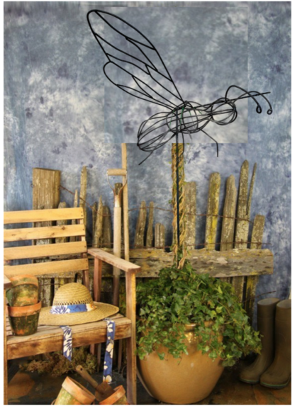 Wire bumble bee topiary frame on a pole above a potted ivy plant, garden props around it