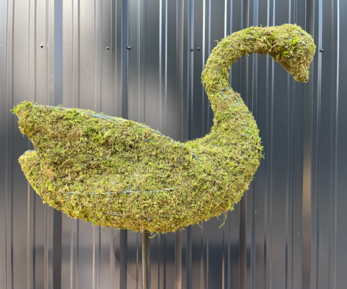 Moss-packed swan topiary on a pole in front of a dark corrugated metal wall