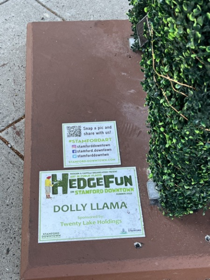 Close-up of the plinth's HedgeFun 'Dolly Llama' sponsor signage next to the foliage