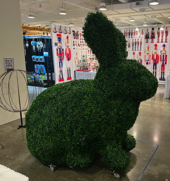 Side view of a life-size rabbit topiary in artificial boxwood, ears up, standing on casters indoors