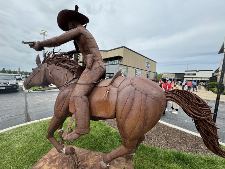 Wide view of the metal cowboy-and-horse sculpture with onlookers nearby