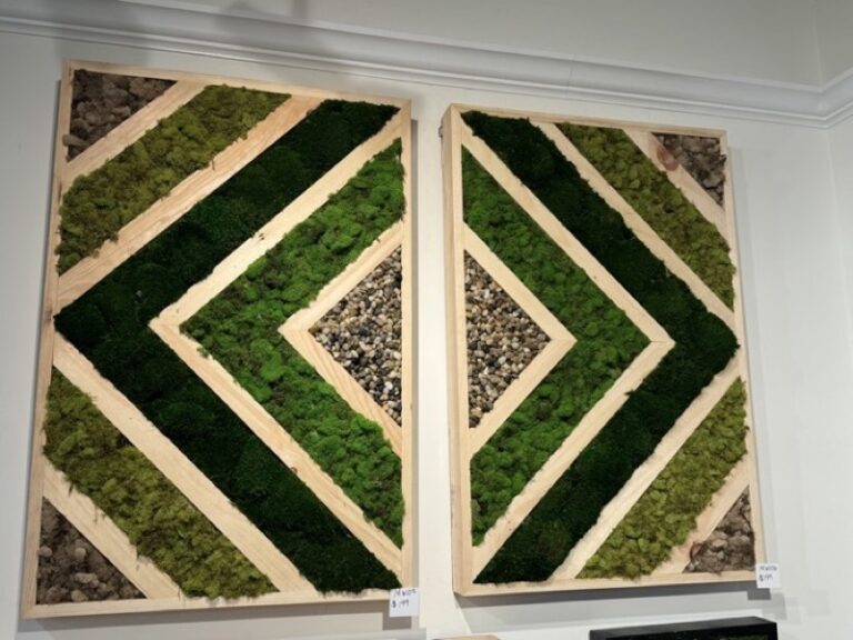 Two moss wall panels in a green diamond and triangle pattern with wood trim and a pebble accent square, mounted on a wall
