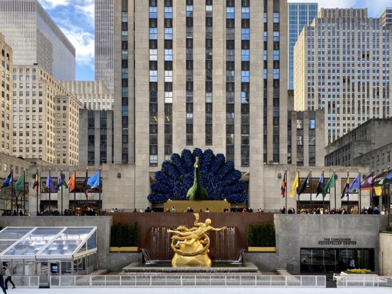 Peacock topiary on display in Rockefeller Plaza with crowds and surrounding buildings