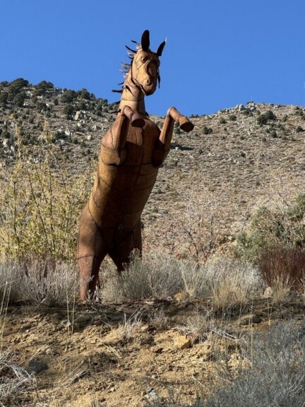Close low-angle view of the horse sculpture's head and raised front legs against blue sky