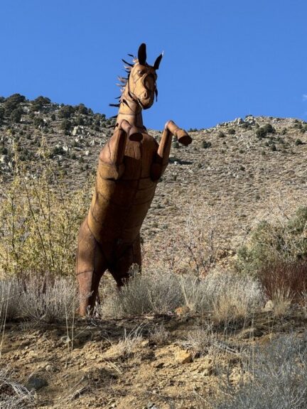 Low-angle view of the metal horse sculpture rearing against a clear sky and rocky hillside