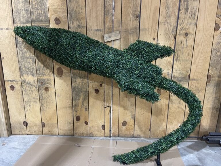 Green foliage-covered rocket topiary lying against a wood plank wall, full nose-to-tail shape visible