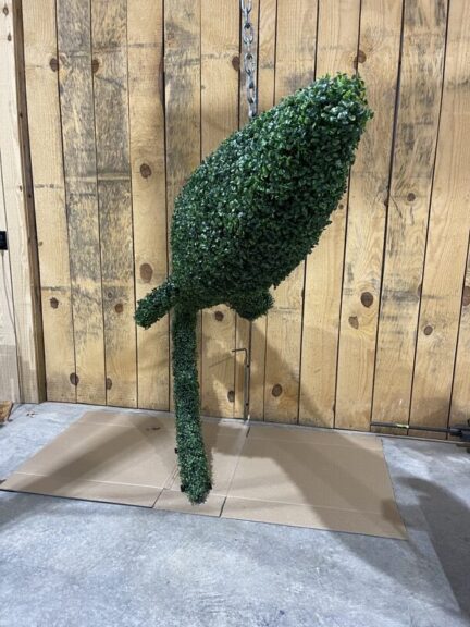 Green foliage-covered topiary shape hanging vertically by a chain, elongated form with a pointed top