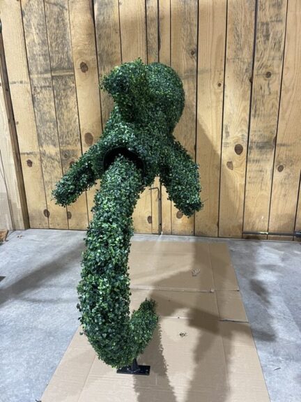 Green foliage-covered topiary shape suspended by a chain hoist, rounded form with an opening at the torso
