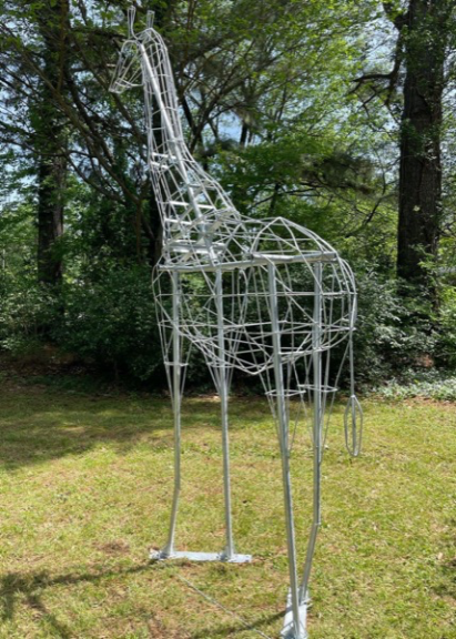 Bare wire giraffe topiary frame standing on grass among trees