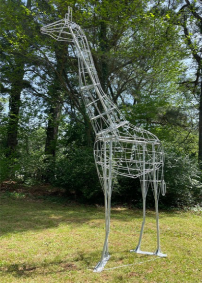 Bare wire giraffe topiary frame standing on grass, side angle