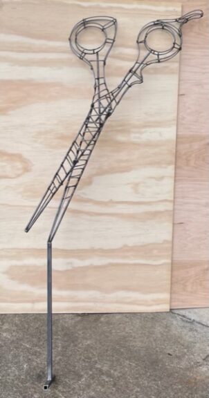 Bare wire-frame scissors topiary armature, without moss, propped against plywood