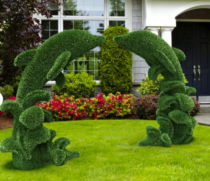 Green dolphin-arch topiary shown in a front yard beside a house entrance and flower bed.