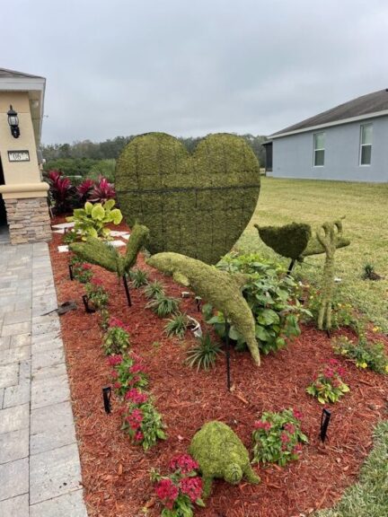 Wider view of the moss scissors topiary in a garden bed with a moss heart and other moss shapes