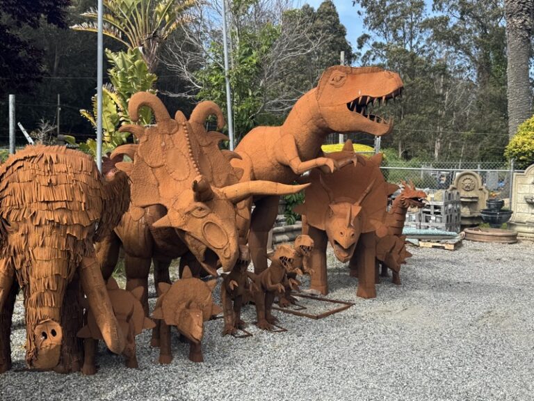 Row of rust-toned metal sculptures including a mammoth, triceratops, T-Rex, and several smaller dinosaur figures
