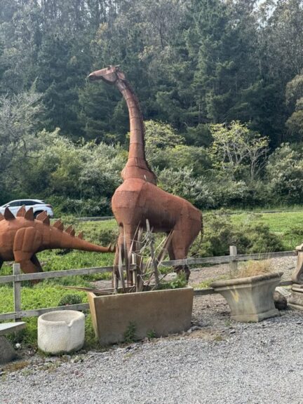 Rusted scrap-metal giraffe sculpture with a raised head, next to planters