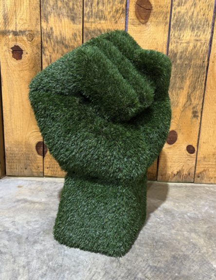 Green artificial-grass raised-fist sculpture, angled view showing the thumb and knuckles
