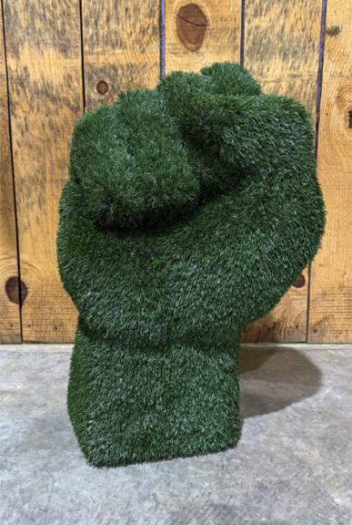 Green artificial-grass raised-fist sculpture against a wood plank wall