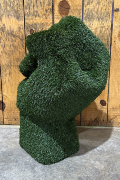Green artificial-grass raised-fist sculpture, side view against a wood plank wall