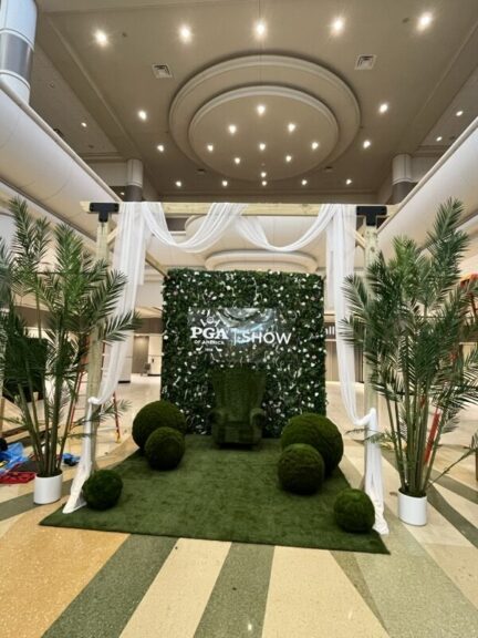 Green-wall exhibit booth with a turf armchair, two moss balls and faux palms, empty before an event.