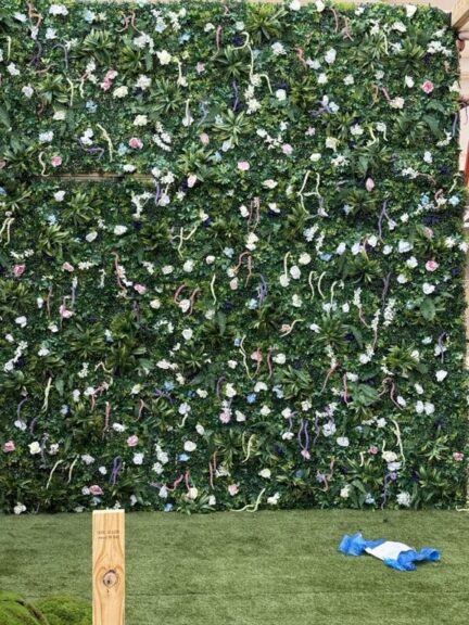Close-up of a finished green wall densely covered in faux flowers and foliage.