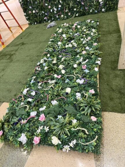 Close-up of a green wall panel with faux flowers laid flat on turf during assembly.