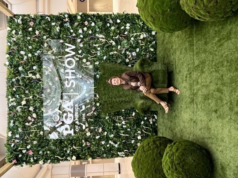 Visitor seated in the artificial turf chair at the PGA Show booth