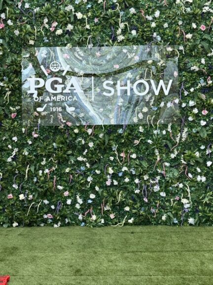 Close-up of an event sign set into a green wall covered with faux flowers and foliage.